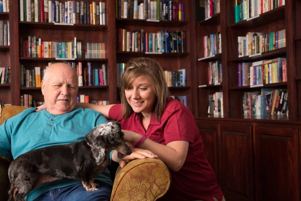 resident with dog and caregiver in library