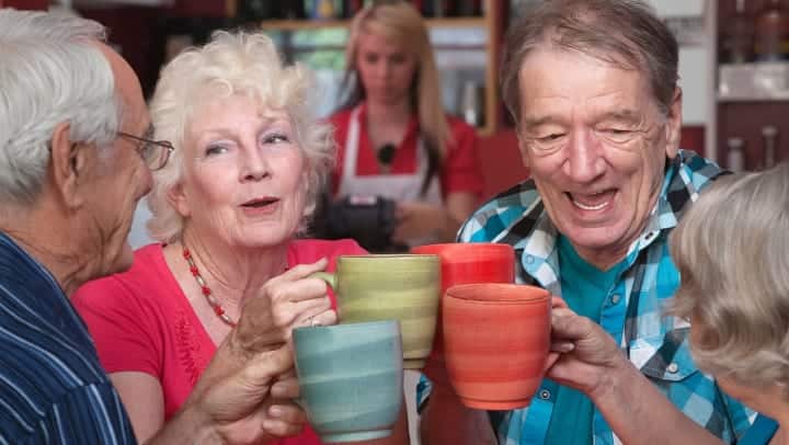 two senior couples clinking coffee mugs together