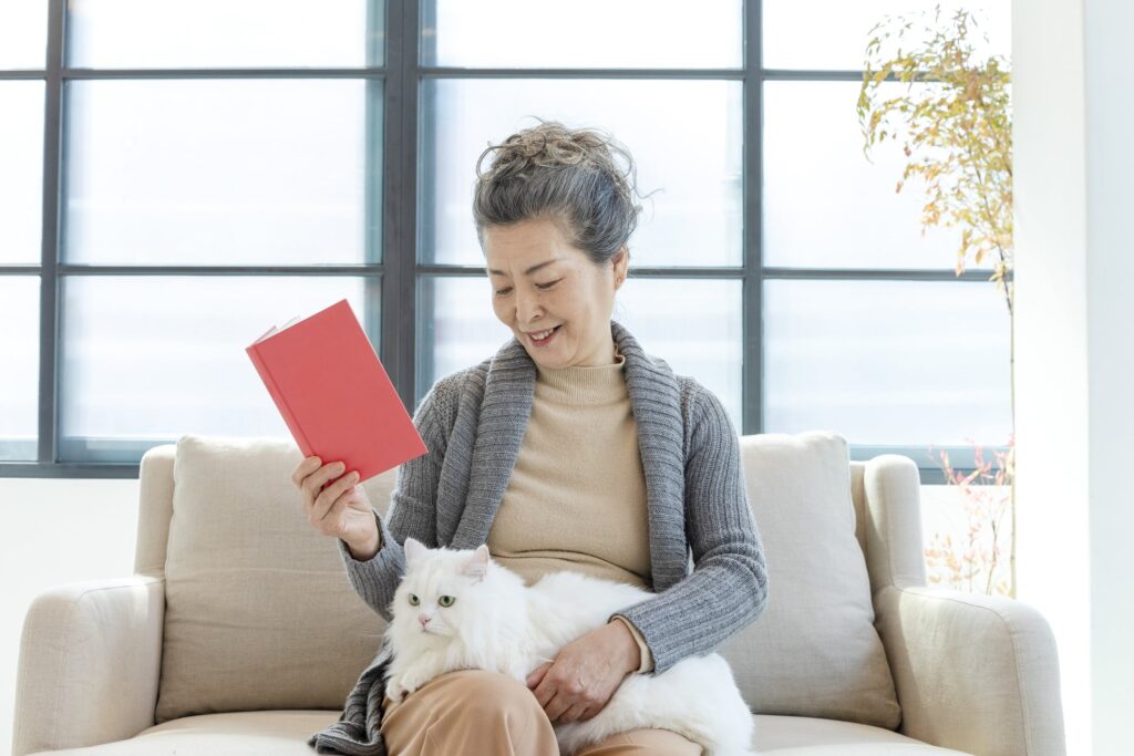 Senior woman sitting on a sofa, reading a book with her cat enjoying the benefits of pet ownership for seniors