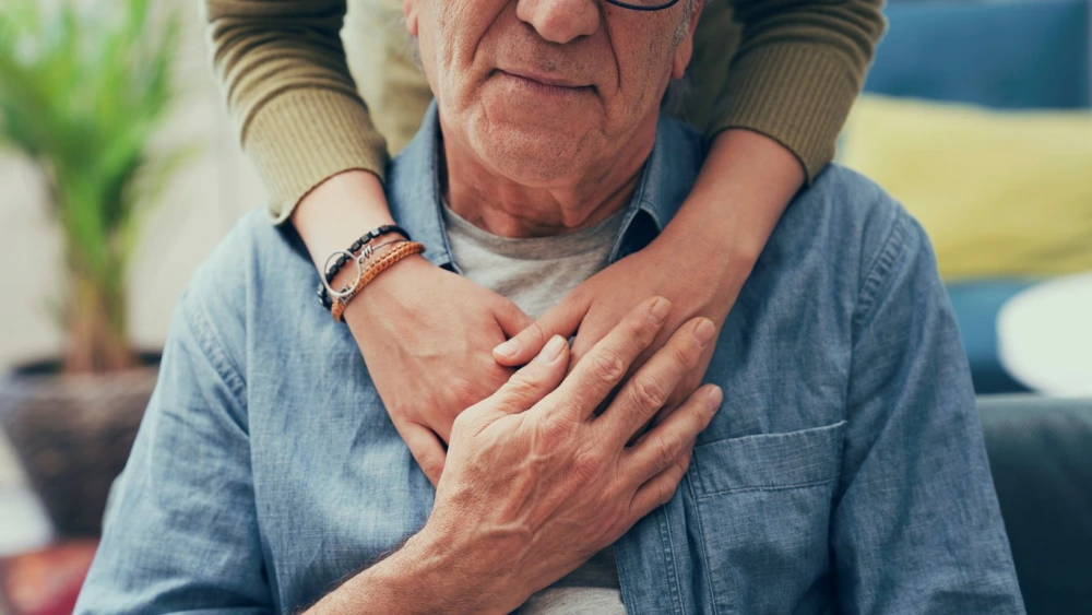 A senior male sitting with a person standing above them with arounds around them