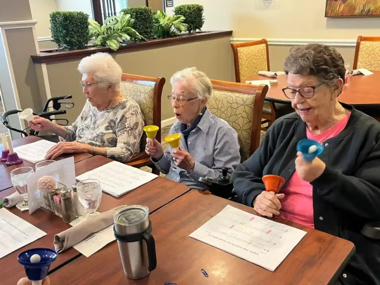 A group of women sitting at a table ringing bells part of music program at The Heritage at Shalimar Gardens retirement home